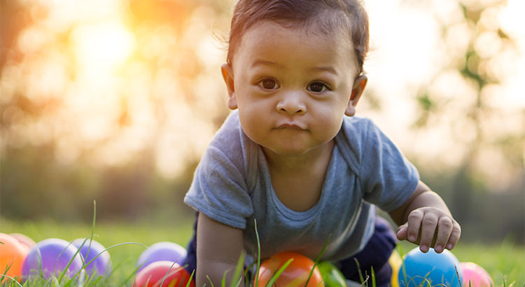 baby crawling in grass with toys