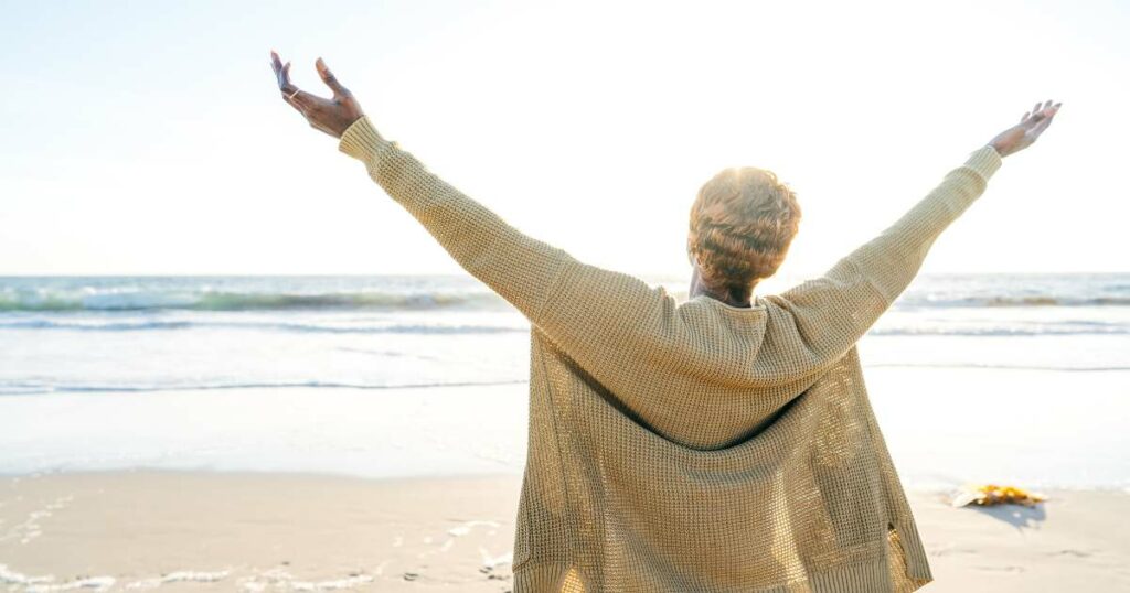 older woman at the beach with her hands in the air